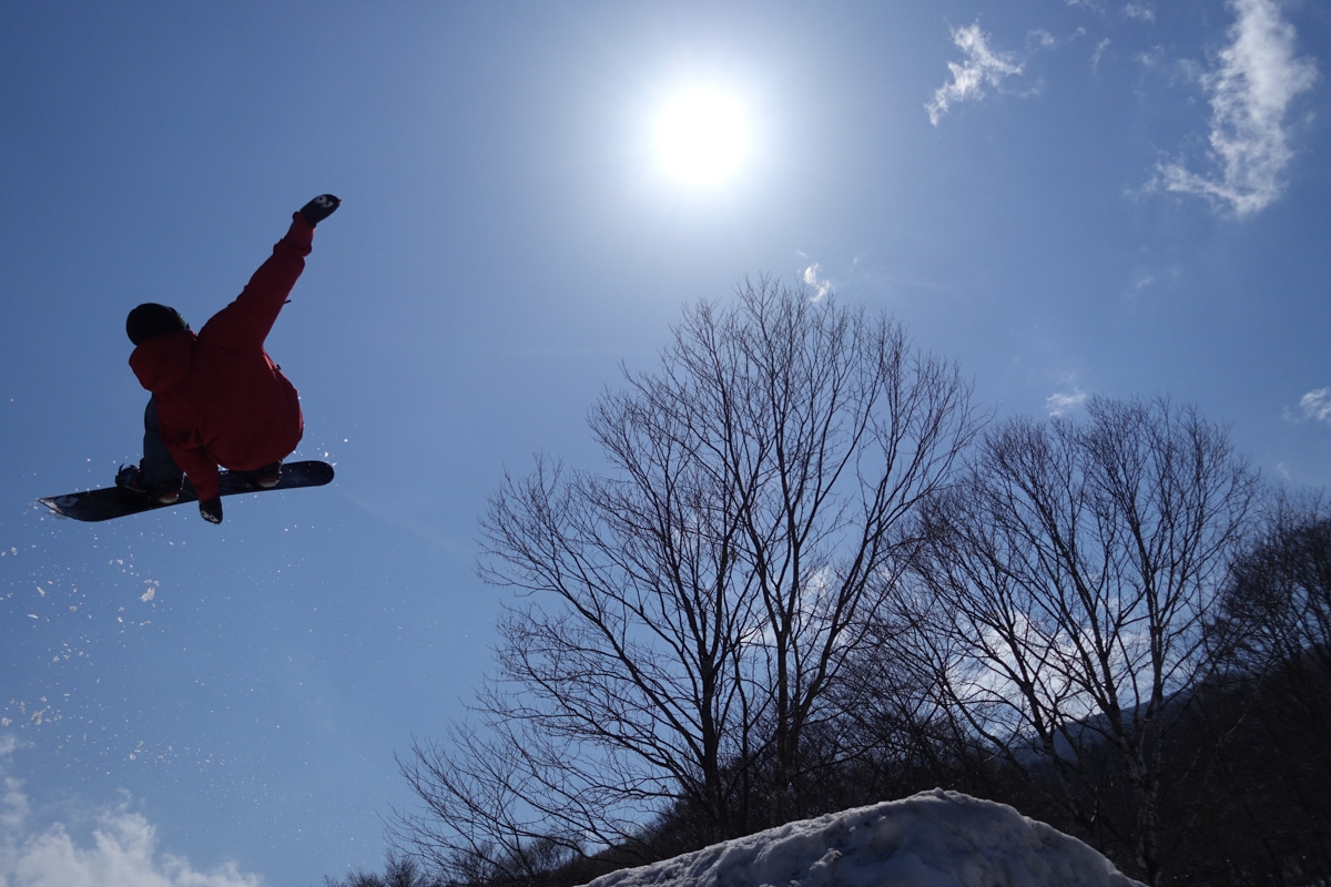 Snowboarder in mid-jump silhouetted against sky with bright sun