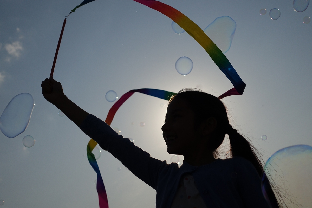 Girl waving streamer in silhouette against sky with bubbles