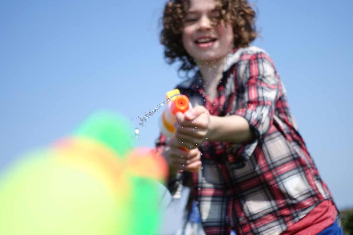 Boy in check shirt shooting water pistol with foreground bokeh