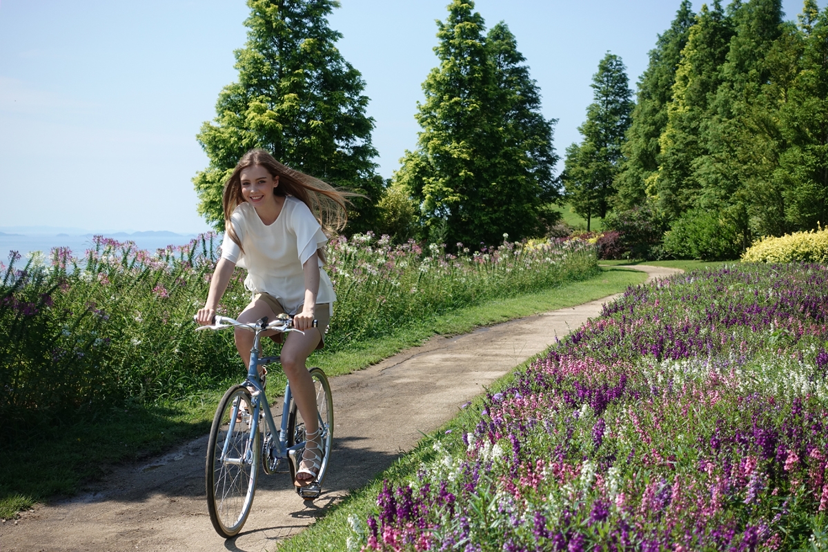 Girl on bicycle riding on path through flower garden