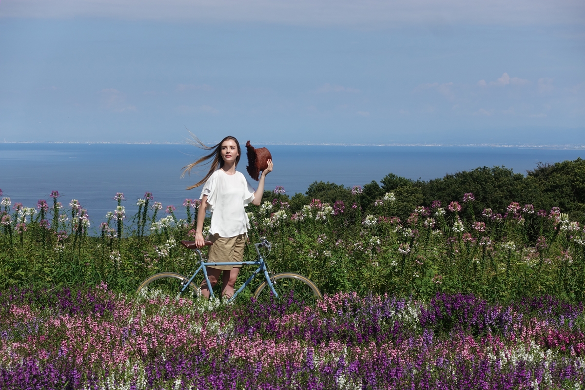 Girl standing with bicycle amid flowers with ocean in background