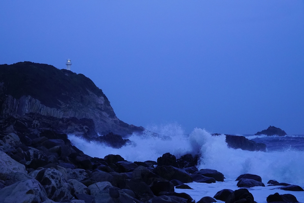 Waves breaking on coastal rocks with lighthouse visible in background