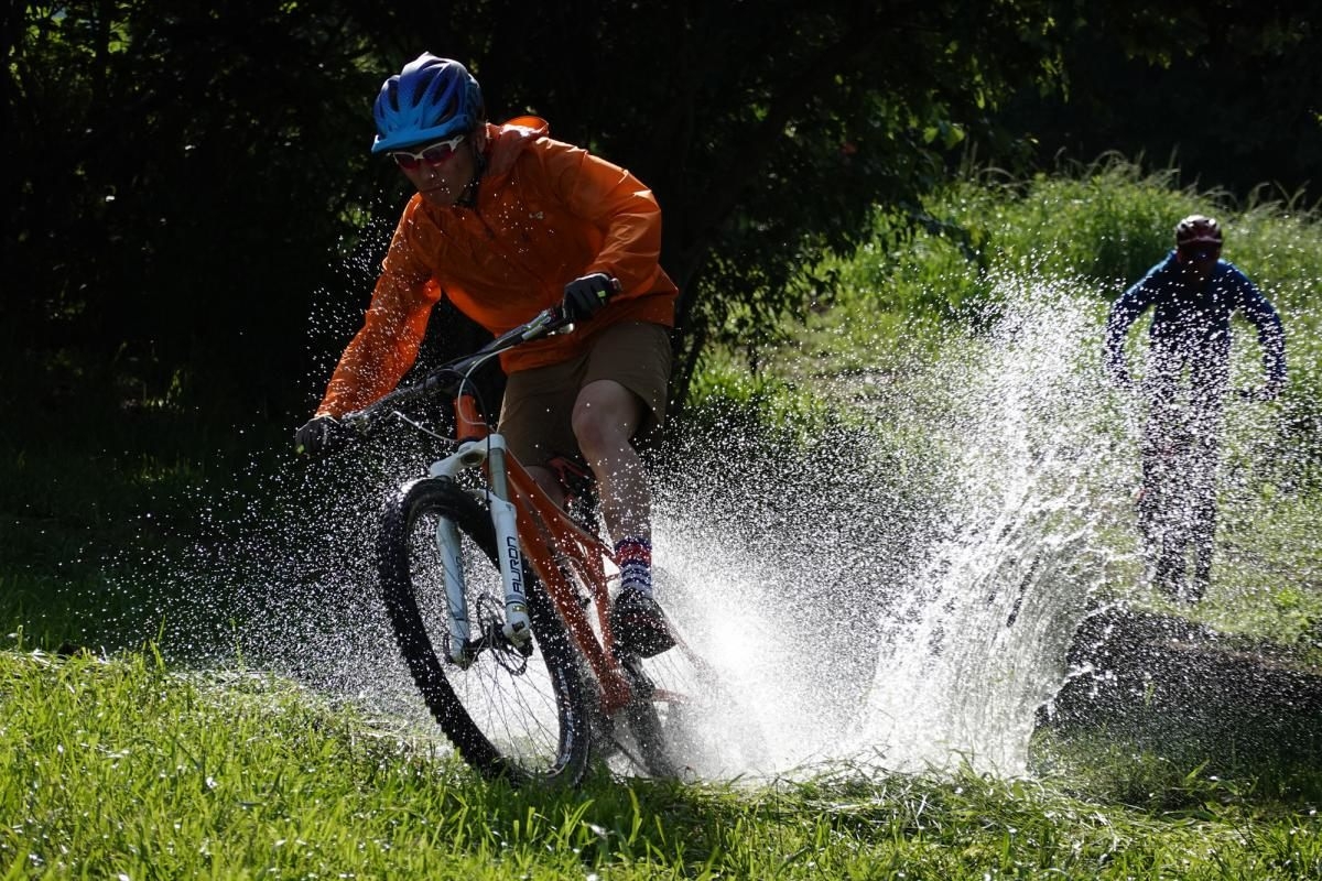 Cycling competitor splashes through water with rival in pursuit in background