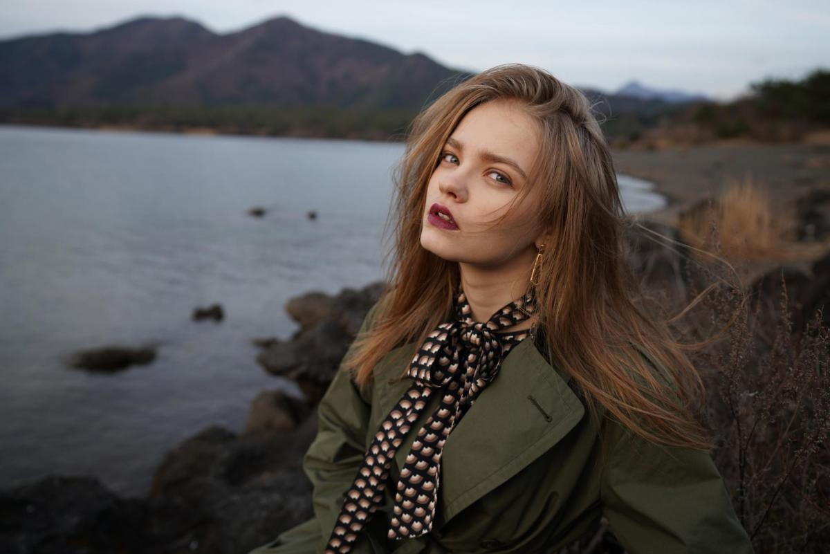 Portrait of woman looking half-sideways at the camera with lake and hills in background