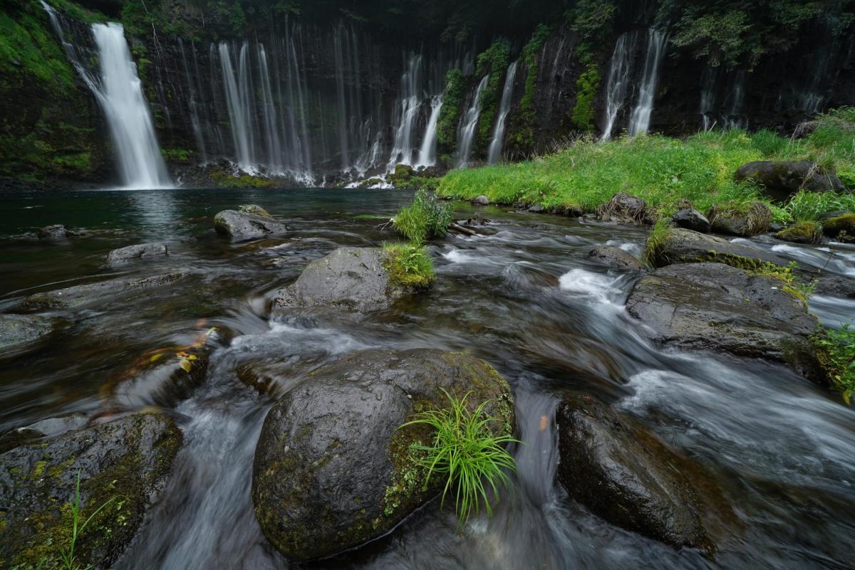 Rocks in flowing stream with waterfall in background