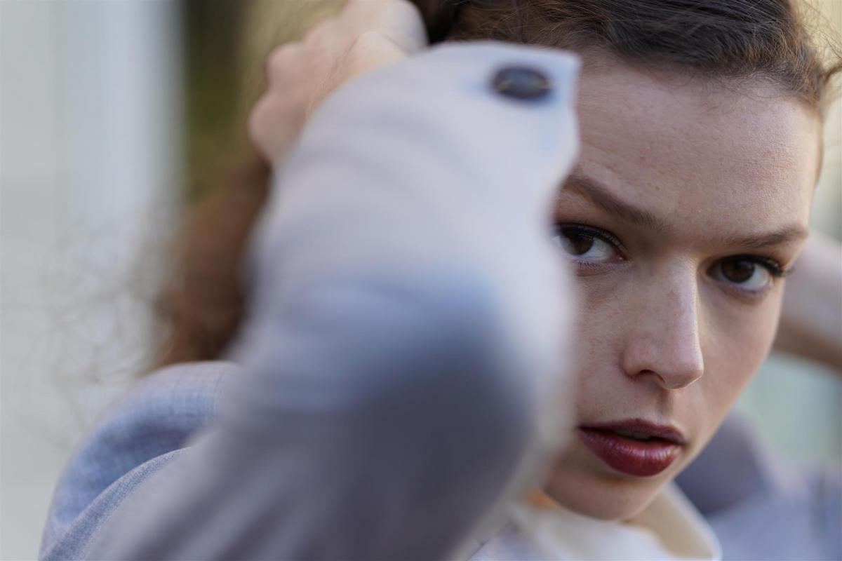 Near-frontal portrait of woman looking at the camera while pulling hair back