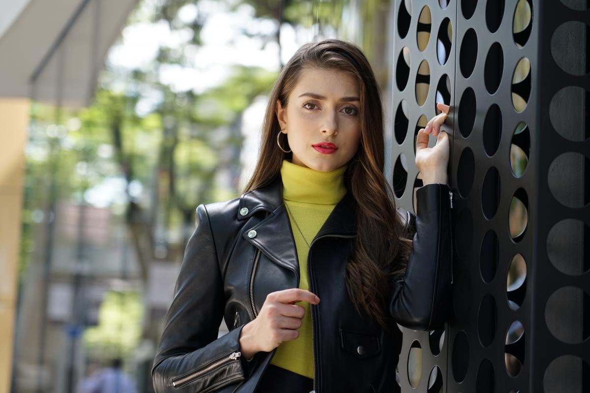 Female model standing next to metal pillar with bokeh background of garden