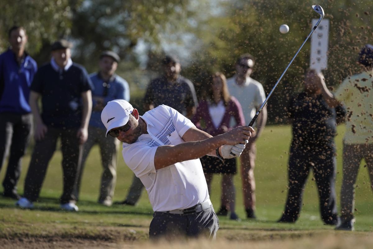 A golfer takes a shot while onlookers water in bokeh background