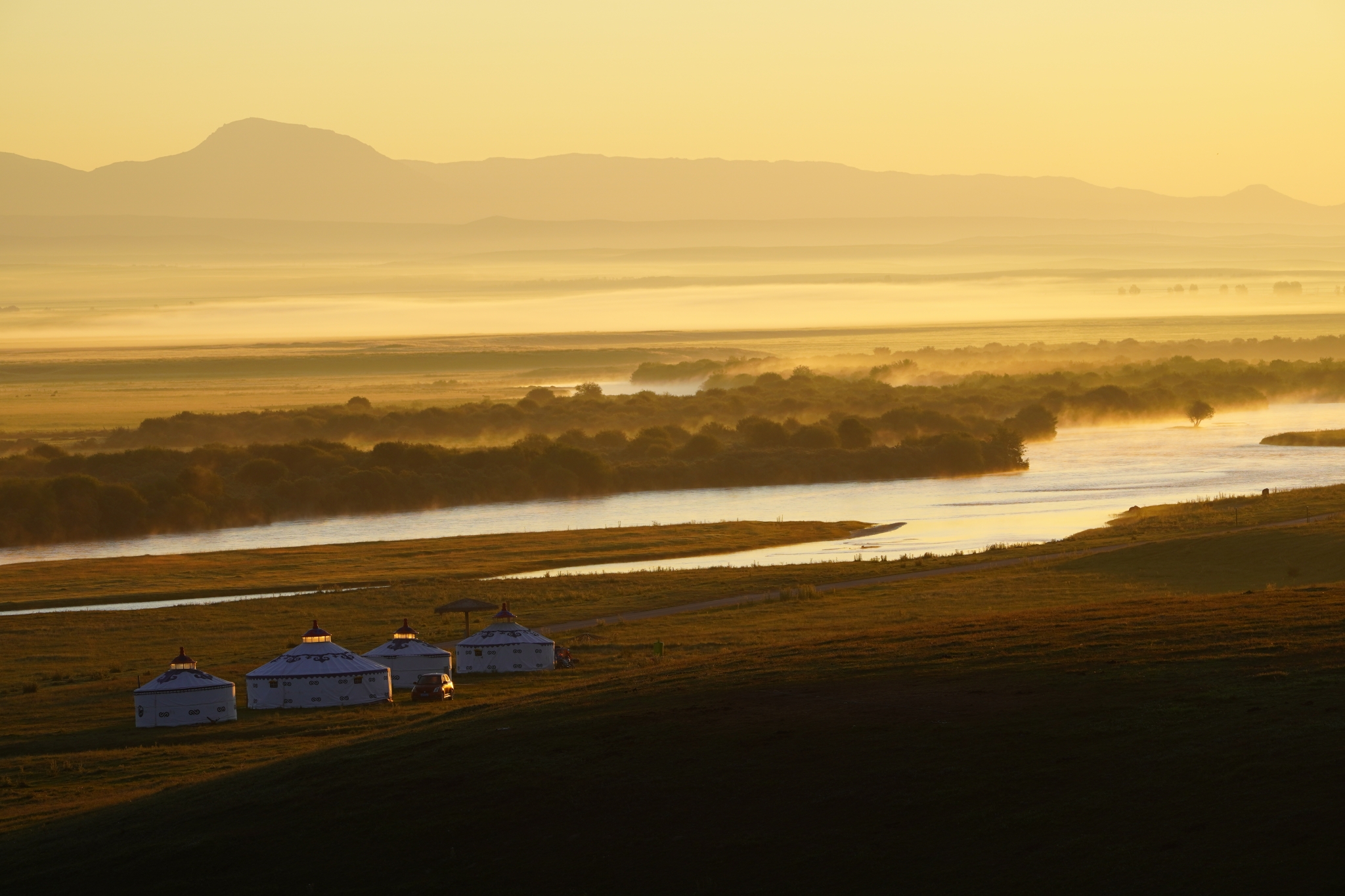 Landscape of wide meandering river at sunset with four white buildings