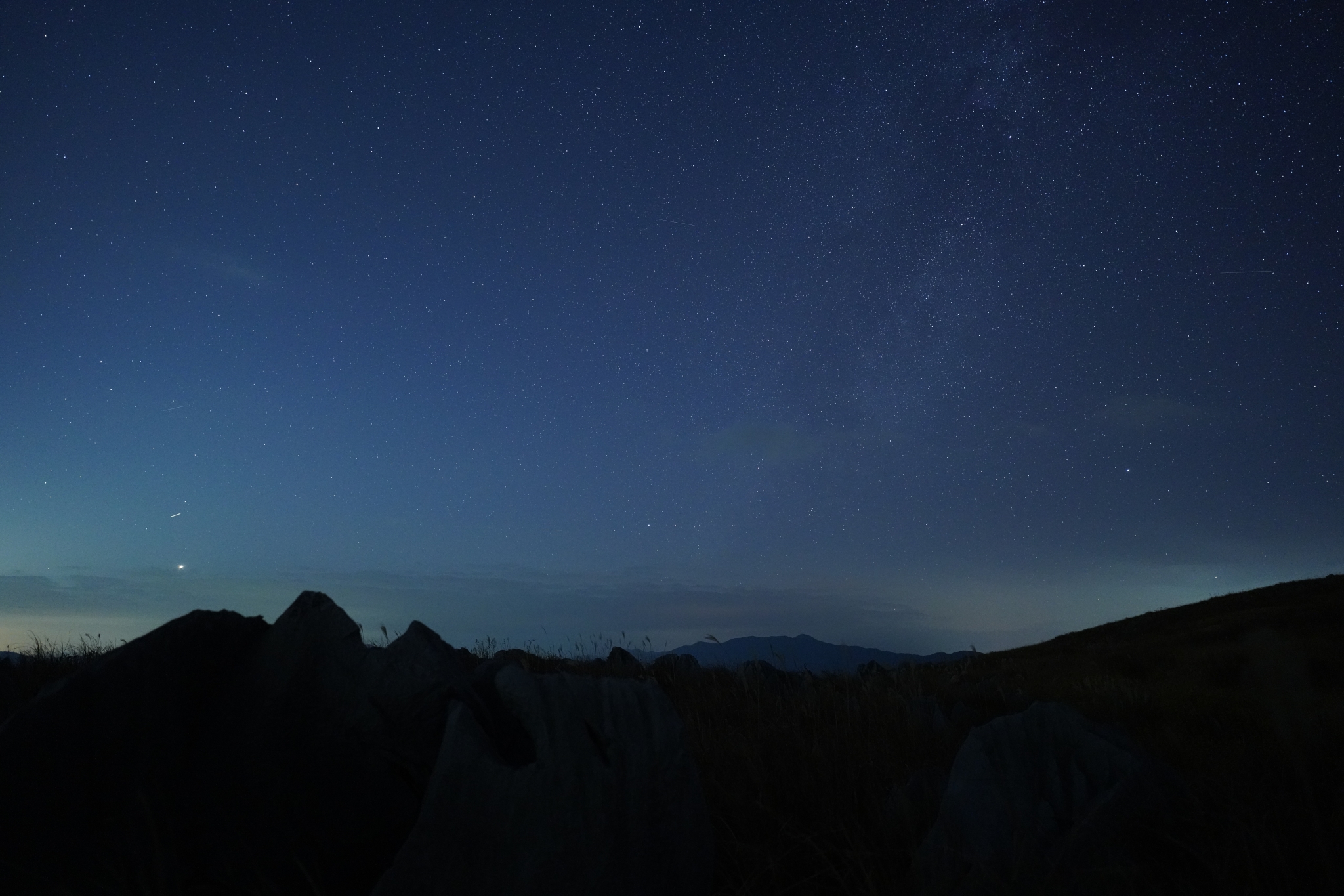 Silhouette of dark hills in front of a deep blue ocean at lowlight