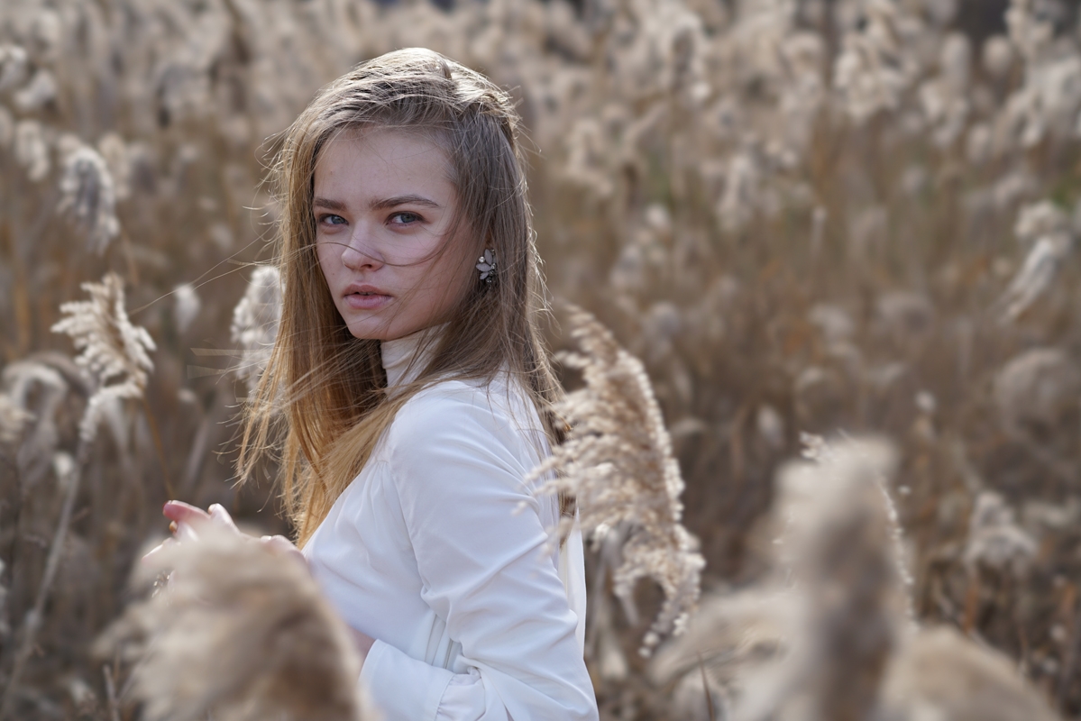 Portrait of woman in field of high grass looking sideways at camera with foreground and background bokeh