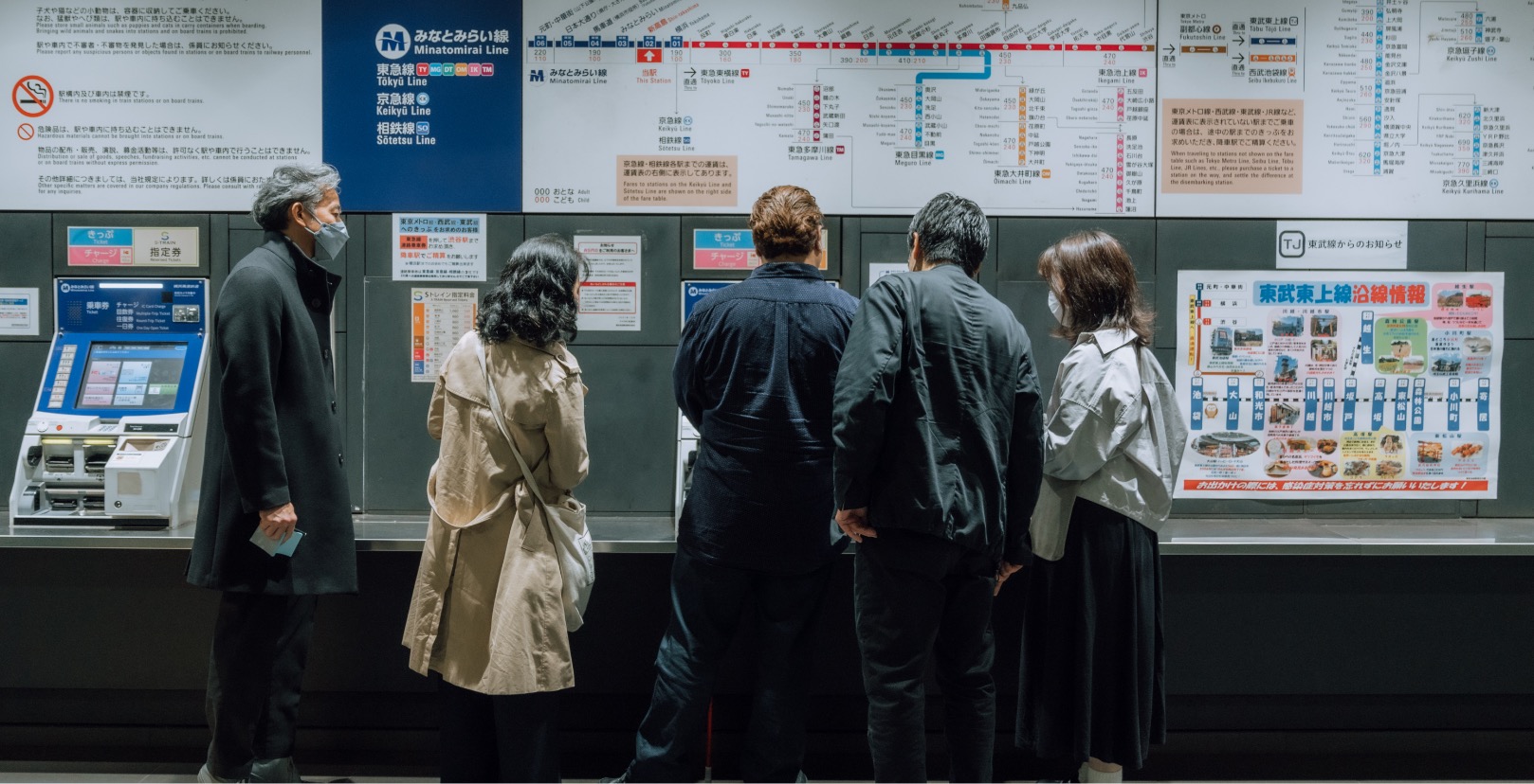 A group of people at the ticketing booth in a train station.