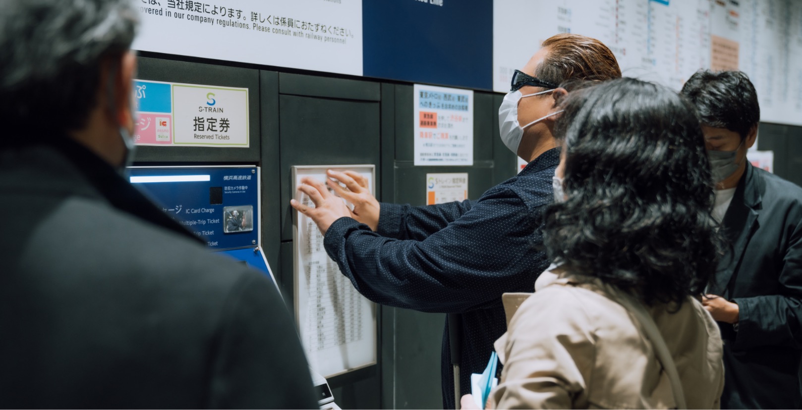 A male with sunglasses touching the price list at a ticketing booth in a train station.