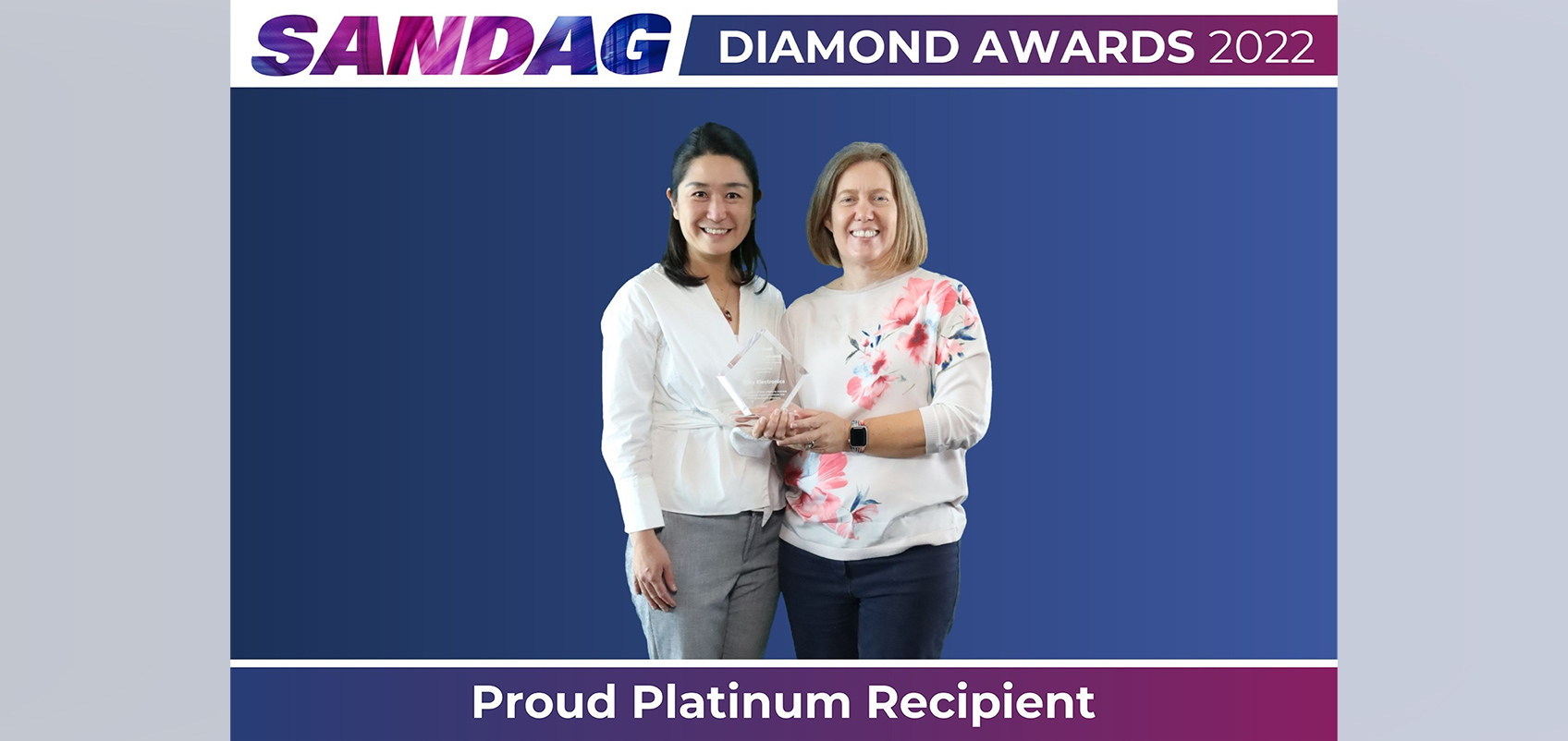 Two employees are holding trophies with "Proud Platinum Recipient" written within the photo