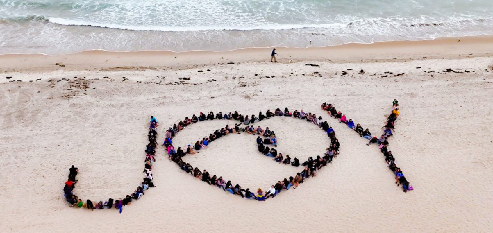 People are lined up on the beach making the word JOY